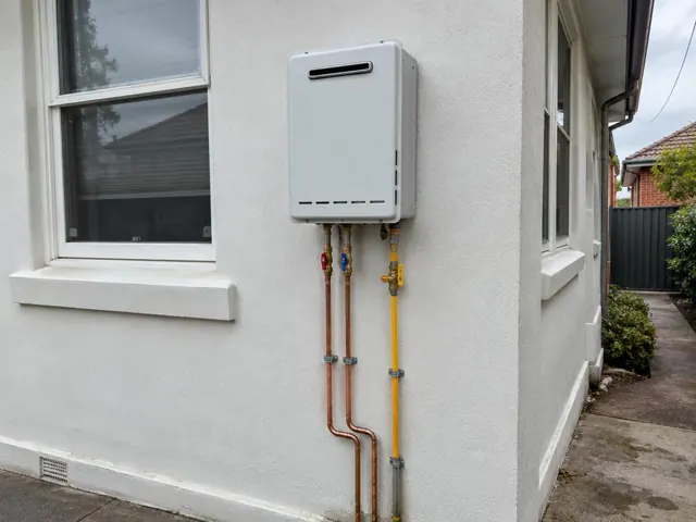 Wall-mounted hot water unit with copper and yellow pipework on an exterior rendered wall in Harris Park